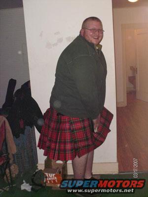 Man wearing a red plaid kilt and a dark green jacket, smiling