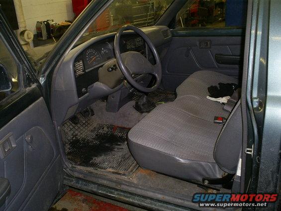 Pickup truck interior with grey fabric seats, dark grey dashboard, and floor mats. A black glove rests on the passenger seat