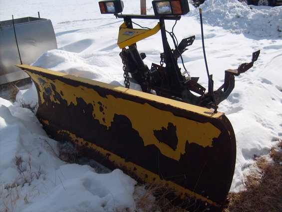 Yellow and brown snow plow with two headlights, partially buried in snow