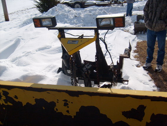 Front view of a yellow snow plow with two headlights, mounted on a vehicle not visible