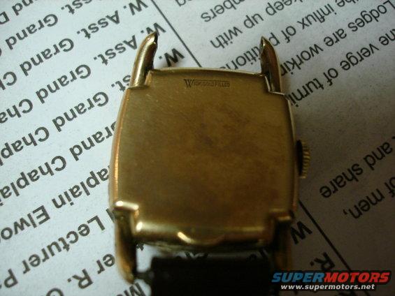 Gold-tone watch case back with "W" logo and text above lug