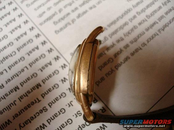 Gold-toned watch case with a cracked crystal, seen from the side against a document