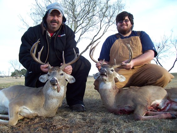 Two hunters pose with two large deer in a field