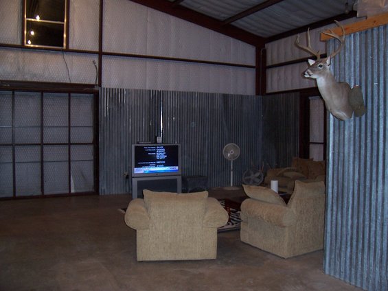 Interior scene with a mounted deer head, two armchairs, a television, and corrugated metal walls