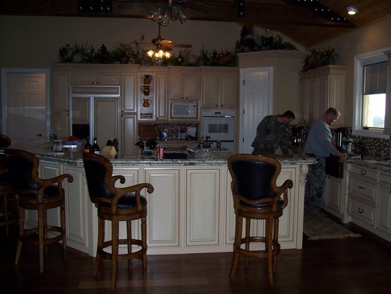 Kitchen with island, bar stools, cabinets, refrigerator, microwave, and two men