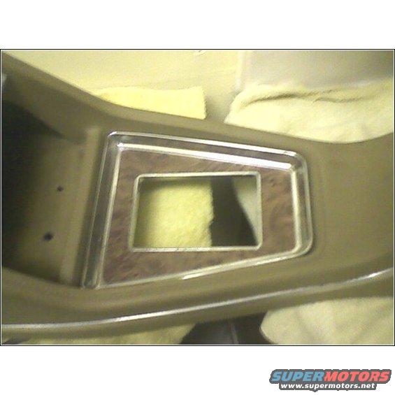 Dashboard trim with wood grain accent and chrome trim around a rectangular opening. The opening reveals yellow foam padding