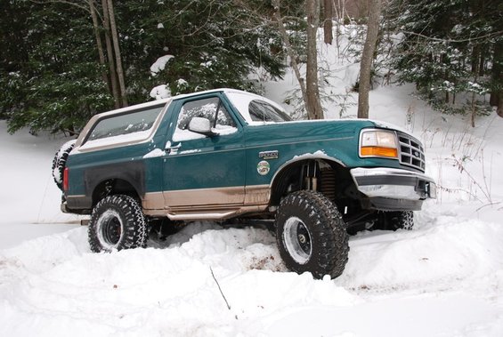 Green 1996 Ford Bronco with tan trim, lifted suspension, and off-road tires stuck in snow