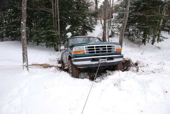 Green 1996 Ford Bronco stuck in snow, being pulled by a winch line