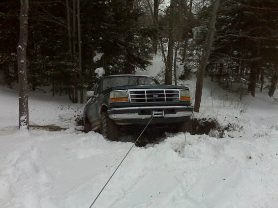 Green Ford F-Series truck stuck in snow, being pulled by a winch line