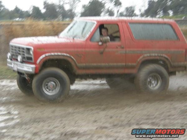 Red Ford Bronco driving through mud, front quarter view