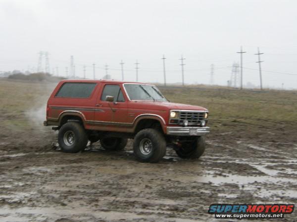 red SUV with lifted suspension driving through a muddy field
