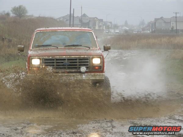 Red Ford Bronco splashing mud, front view, covered in dirt