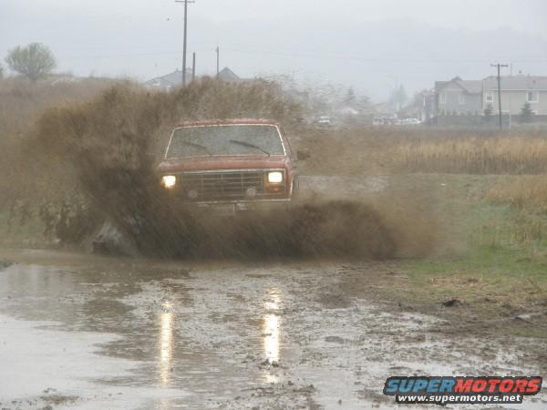 Red 1980s Ford Bronco kicking up mud