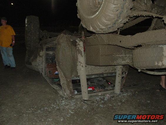 Mud-covered truck flipped on its side with a spare tire visible underneath