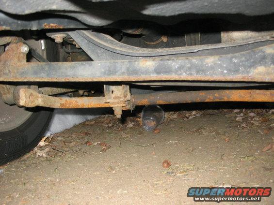 Undercarriage view of a car with rusty suspension components and a glass jar on the ground
