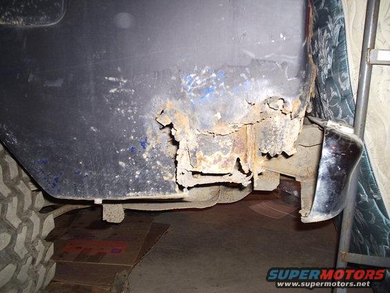 Close-up of heavily rusted metal on the lower rear quarter panel of a vehicle, with a tire visible on the left