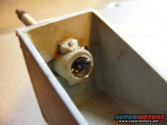 Headlight socket with rust and a metal post protruding from a white plastic housing