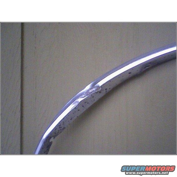 Chrome trim piece with dents and rust spots against a wood-paneled background