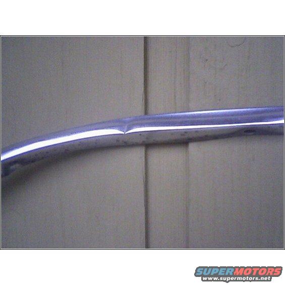 Chrome trim piece with a dent against a light-colored wall