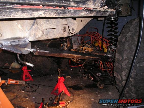 Vehicle frame and suspension components are visible, with tools and equipment around. It's on jack stands