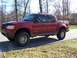 2002 Ford Sport Trac - A red Ford Explorer Sport Trac pickup truck is shown from a 3/4 front angle on a paved road with trees in the background.
