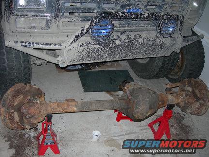Front axle assembly resting on red jack stands, with the front bumper and tires of a vehicle above