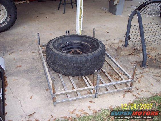 Spare tire on a metal rack, with a portion of a vehicle tire visible on the left