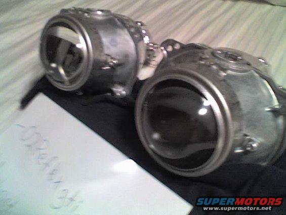 Two silver projector headlights with black lenses on a dark cloth