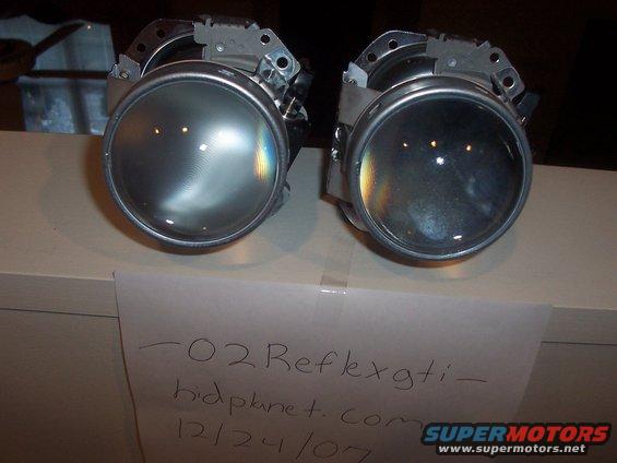 Pair of projector headlight assemblies on a shelf with a handwritten note