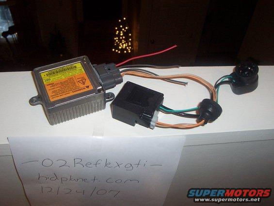 Car part with wires and connectors, possibly an airbag module. Text on paper says "-02 Reflexgti- kidplanet.com 12/24/07"