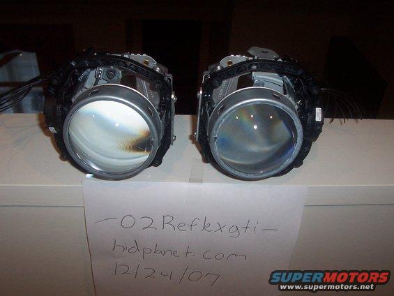 Two disassembled projector headlights with wiring, resting on a surface with a handwritten note