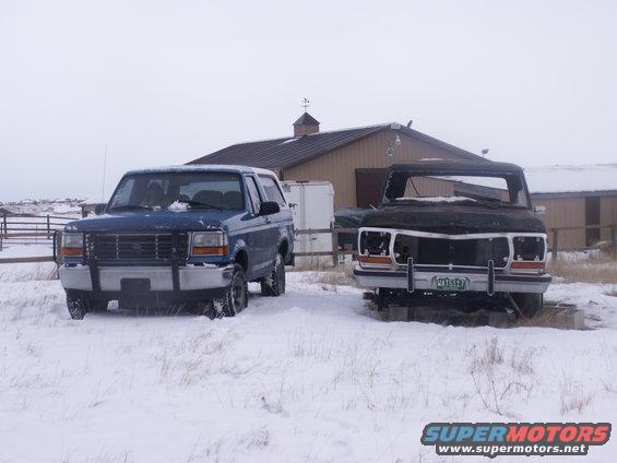 Blue 1992 Ford Bronco and a dark, damaged truck in a snowy field