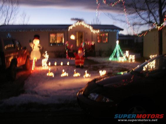 Two vehicles parked in front of a house decorated for Christmas with inflatable figures and lights