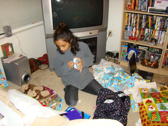 Girl opening presents in a room with a TV and bookshelf
