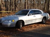 Silver 2002 Lincoln Town Car parked on a dirt road with trees in the background