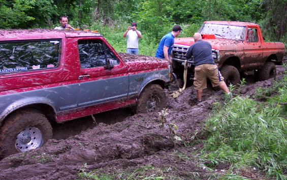 Red 1995 Ford Bronco being pulled from mud by orange truck
