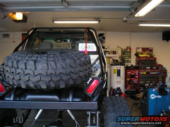 Spare tire on rear carrier of off-road vehicle, license plate reads 'ROHRSE'. Garage interior with tools and water heater visible
