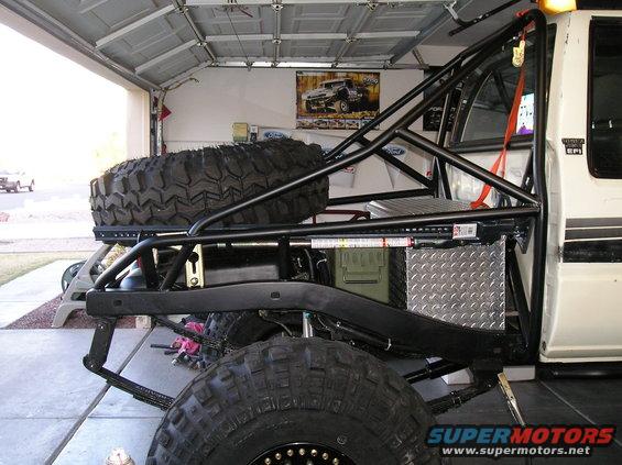 White off-road truck with roll cage, spare tire mounted on rear, and large tires