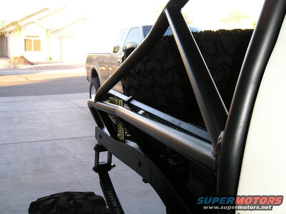 Off-road truck bed with spare tire and roll cage, another truck in background