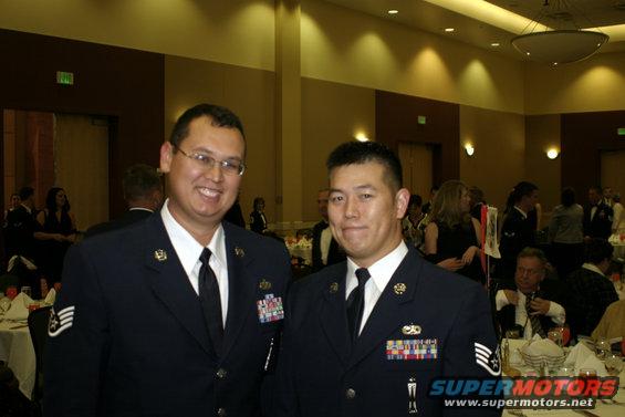 Two men in military dress uniforms smile for the camera at an indoor event