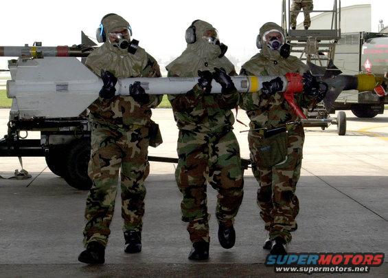 Three soldiers in hazmat suits carry a missile on an airfield