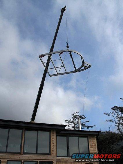 crane lifting a large, curved window frame over a building
