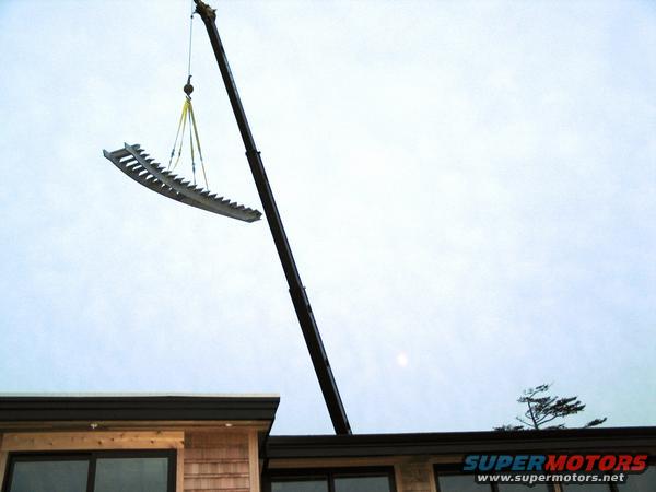 Crane lifting a metal rake-like object over a building