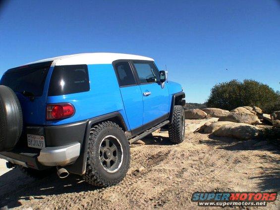 Blue and white 2007 Toyota FJ Cruiser from rear, parked on dirt road with rocks