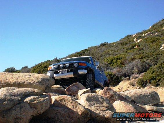 Blue 2007 Toyota FJ Cruiser navigating a rocky trail with auxiliary lights on the front grille