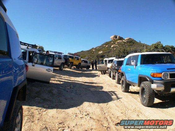 Several 2007 Toyota FJ Cruisers parked in a line on a sandy dirt road with a hill in the background