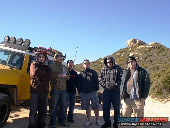 Yellow SUV with roof lights and a group of guys standing in front of a hill
