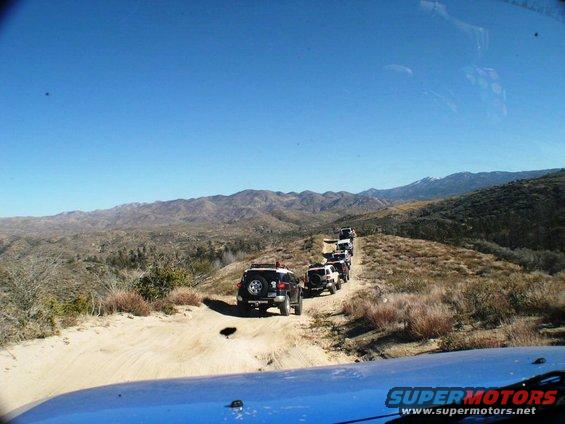 Line of white and dark Toyota FJ Cruisers driving on a dirt road in a mountainous, arid landscape