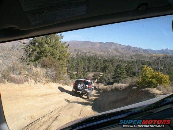 Rear view of a white Toyota FJ Cruiser on a dirt road with mountains in the background