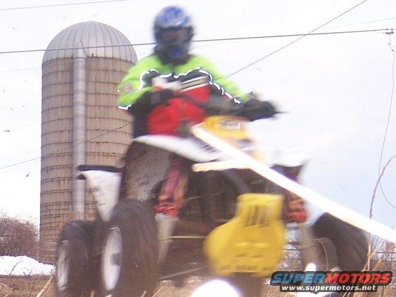 Yellow and white ATV with rider in neon jacket, near a silo